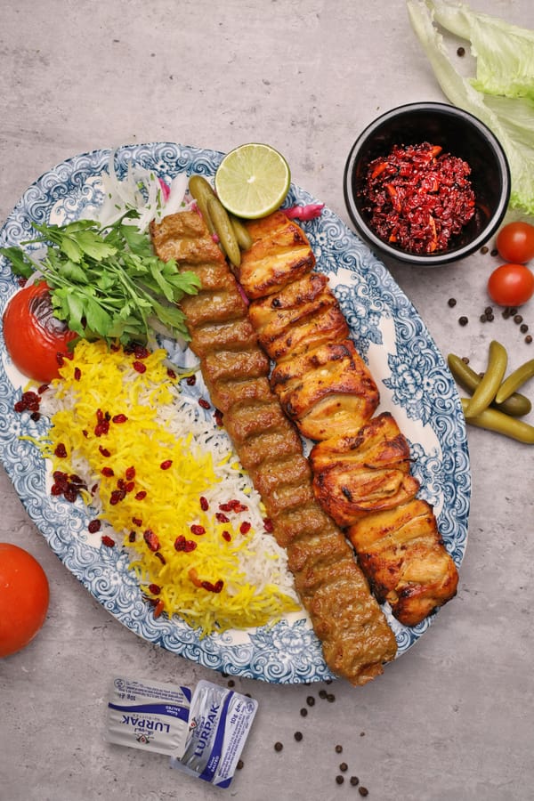 Restaurant-style Persian Koobideh and Joojeh kabab on a blue patterned platter with saffron rice and condiments